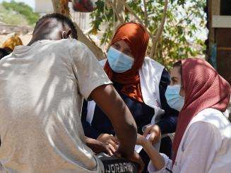 MSF staff members wearing face masks, headscarves, and white vests speak to a man with back turned in Libya. 