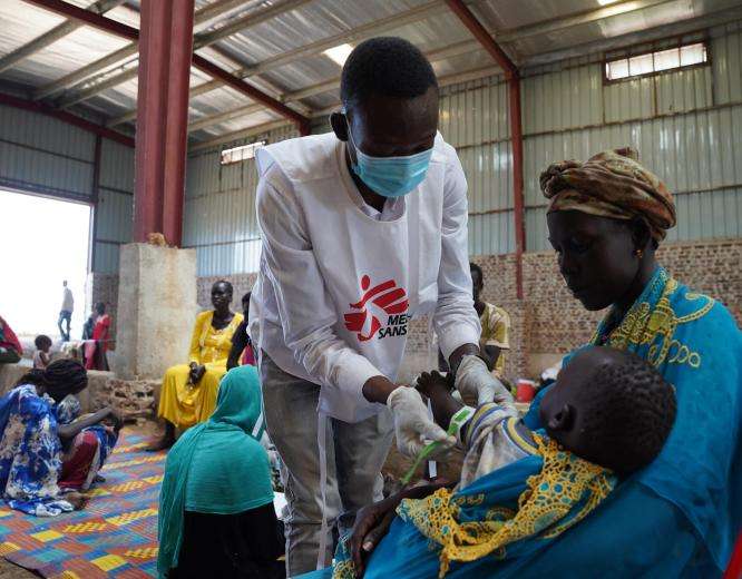 MSF medical staff in white vest treats a Sudanese refugee mother with child in South Sudan.