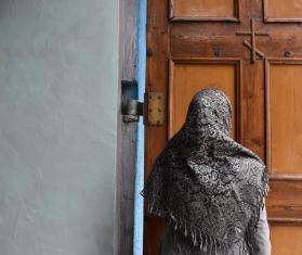 The back of an MSF patient wearing a shawl, standing in front of a wooden door in Belgorod, Russia.