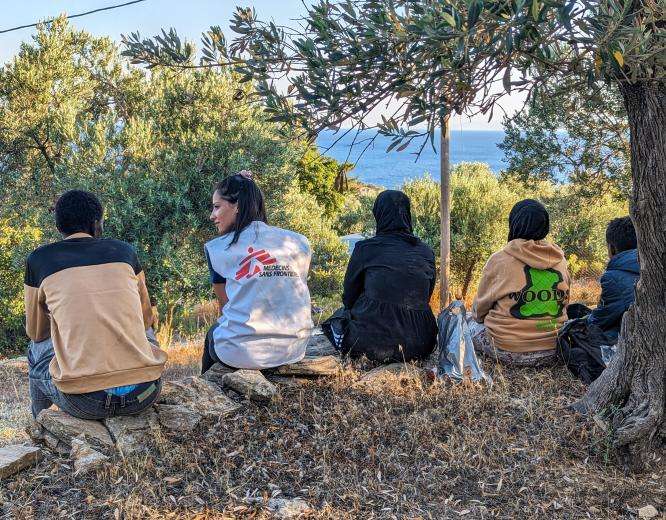 An MSF staff member sits with migrants on a hilltop in Lesvos, Greece.