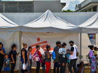 A group of migrants standing on a line under an MSF tent in Danlí, Honduras.