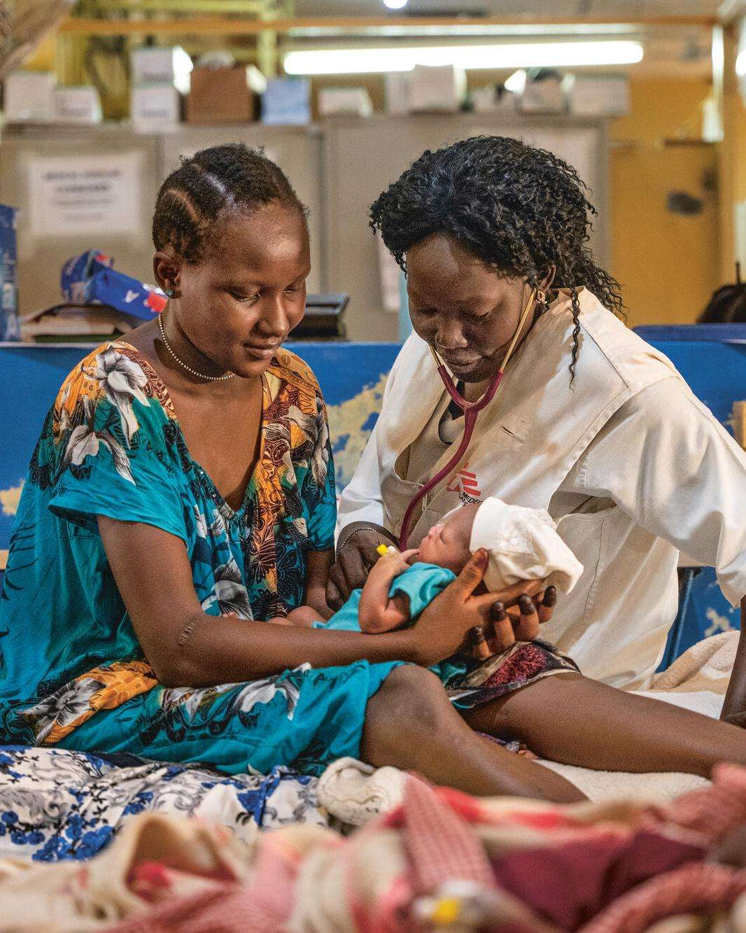 An MSF nurse and patient sit on a hospital bed with a newborn baby in Aweil, South Sudan.