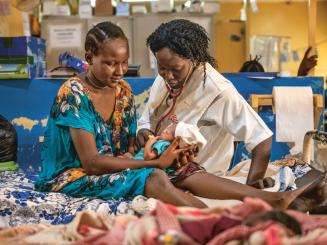 An MSF nurse and patient sit on a hospital bed with a newborn baby in Aweil, South Sudan.