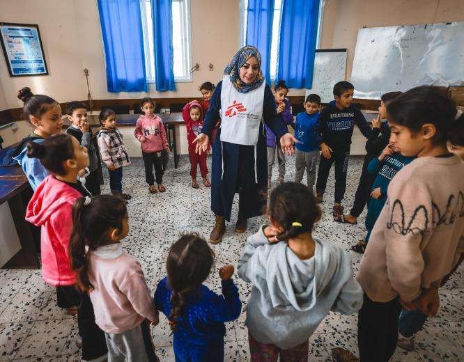 An MSF psychologist stands at the center of a circle of Palestinian children in a mental health session in Gaza.