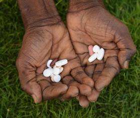 Medication pills in the palms of a person's hand against grass.