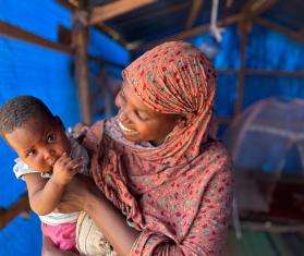 A Sudanese woman holds her child smiling in Chad.