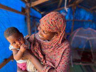 A Sudanese woman holds her child smiling in Chad.