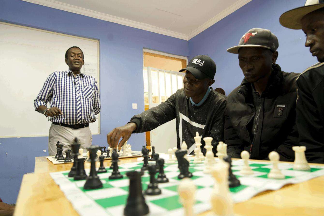 Coach Patrick (standing) teaches patients chess at the Karuri medically assisted therapy clinic empowerment center.