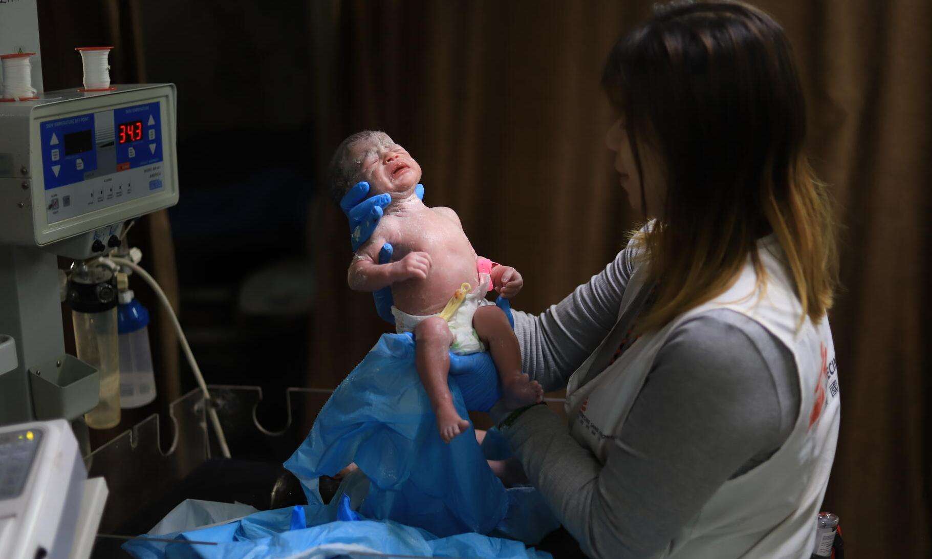 An MSF staff member in Gaza holds up a newborn baby at Nasser Hospital.