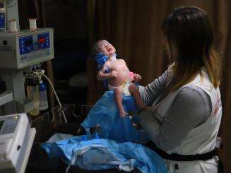 An MSF staff member in Gaza holds up a newborn baby at Nasser Hospital.