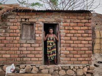 A woman standing in the doorway of her brick home in Malawi.