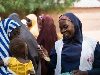 MSF health promoter lets a child taste test Tom Brown, a nutrient-rick porridge, in Nigeria. 